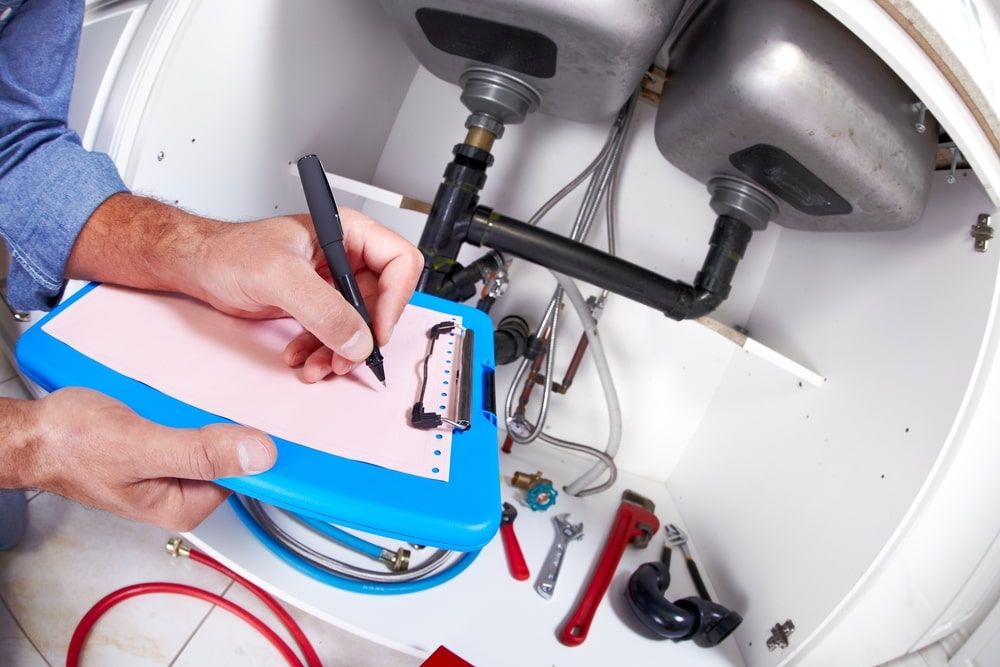 A Plumber Is Writing On A Clipboard While Working On A Sink — Chad Taylor Plumbing In Forster, NSW