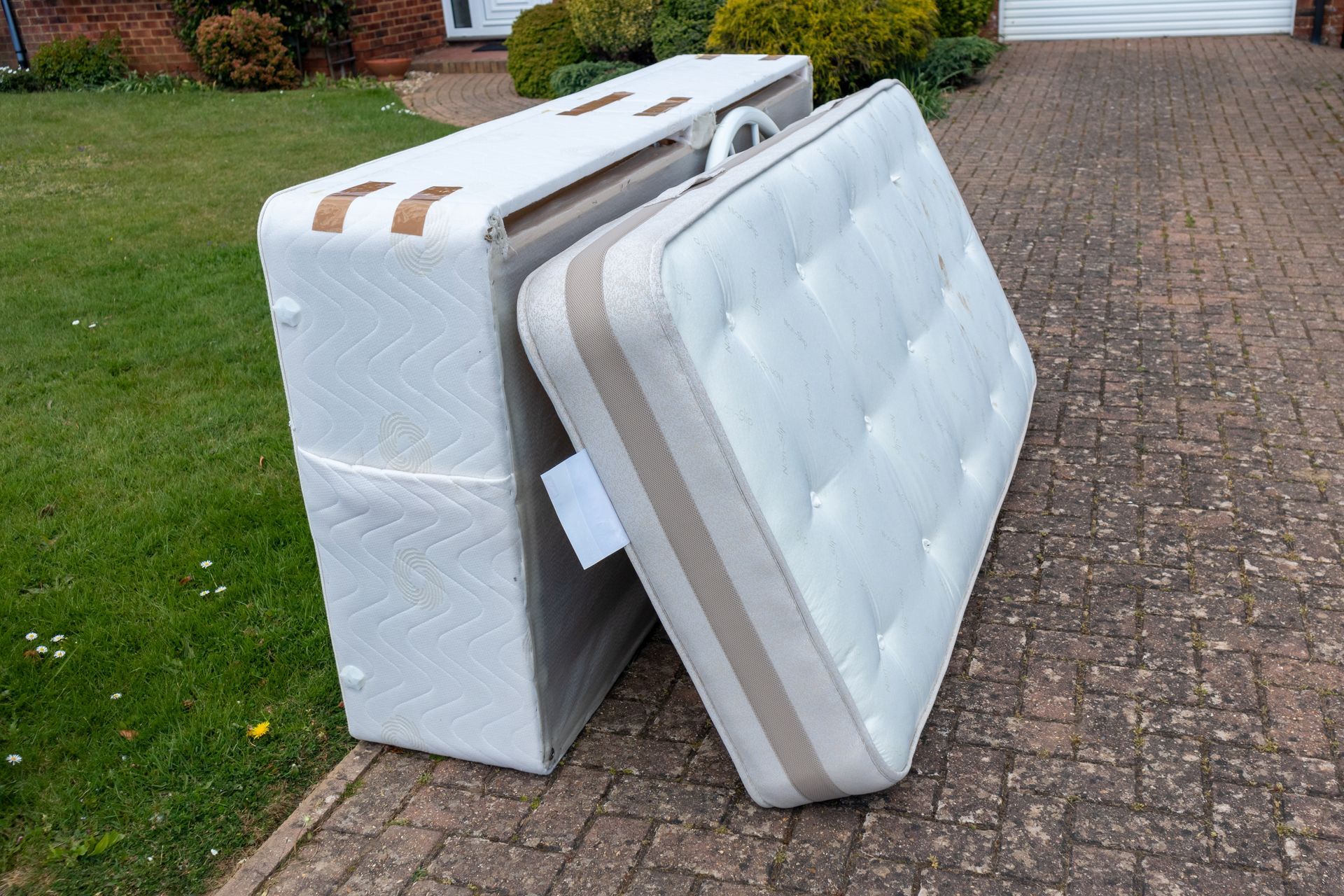 Two mattresses are stacked on top of each other on a driveway.