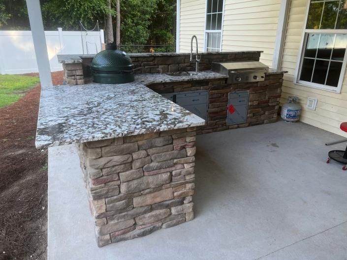 Outdoor kitchen with stone veneer and granite countertop; includes grill, sink, and Big Green Egg.