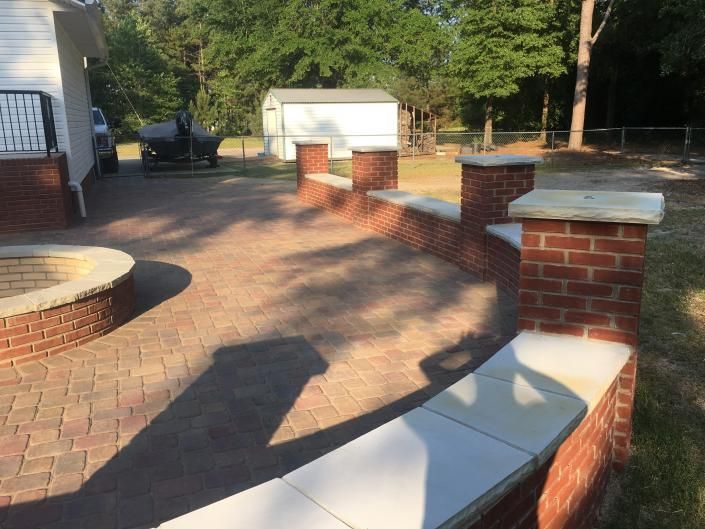 Brick patio with curved wall, pillars, and paved surface; backyard setting.