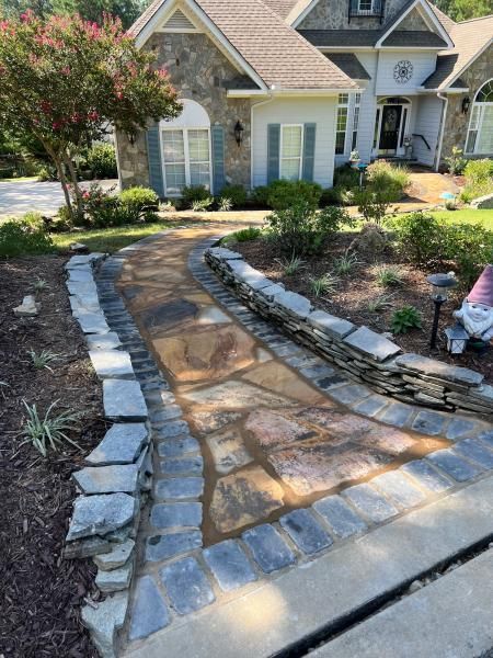 Stone pathway leading to a house with a stone and light blue exterior, lined with garden beds.