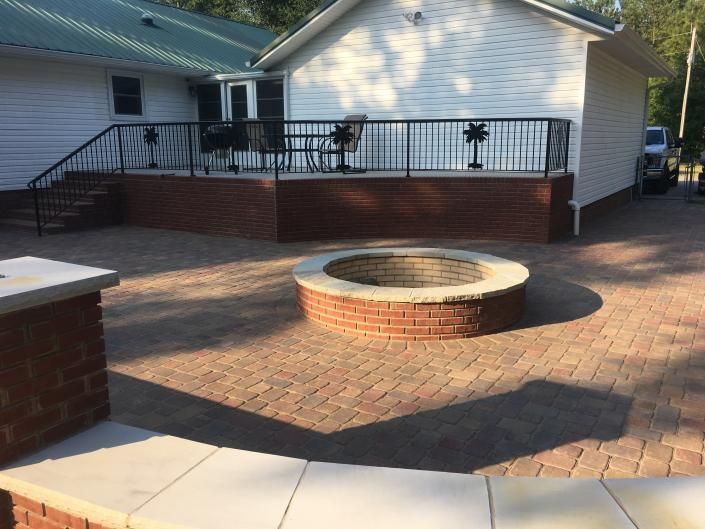 Brick patio with fire pit, raised deck with black railing, and white house in the background.