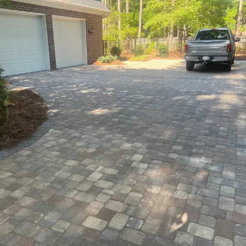 Brick driveway leading to a garage with two doors. A silver truck is parked on the driveway.