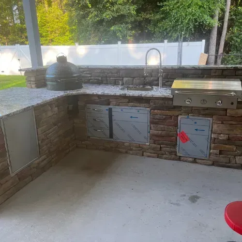 Outdoor kitchen with stone facade, grill, sink, Big Green Egg, and cabinets.