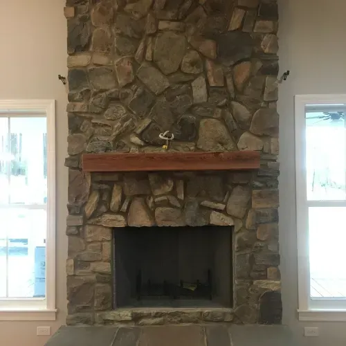 Stone fireplace with wood mantel, flanked by two windows.