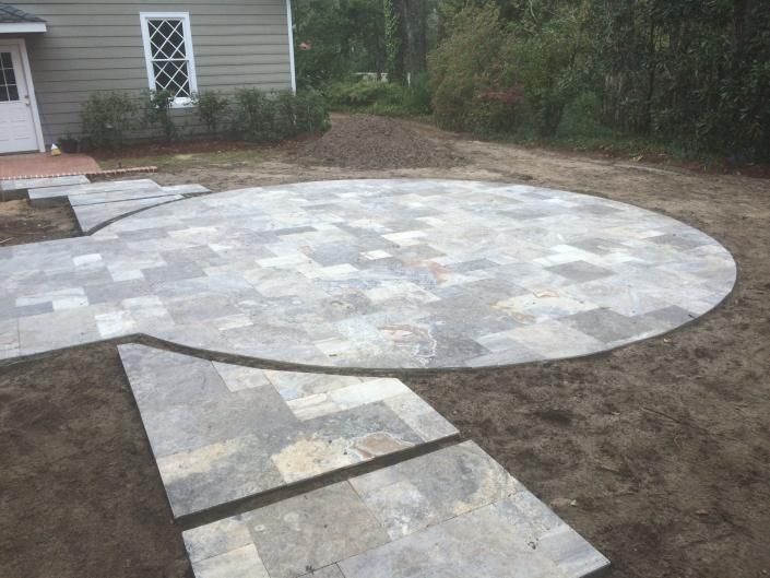 A circular patio made of gray pavers under construction in a yard.