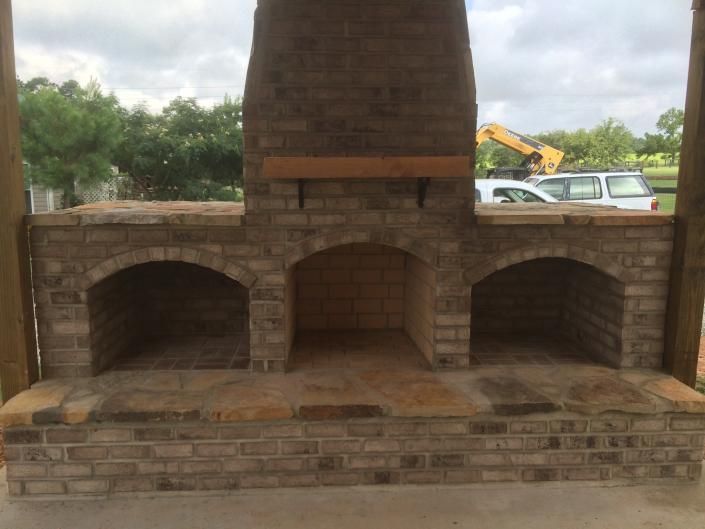 Brick outdoor fireplace with three arched openings and a wooden mantle.