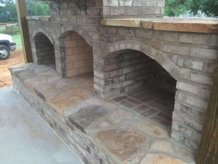 Brick outdoor kitchen with three arched openings and stone counter.