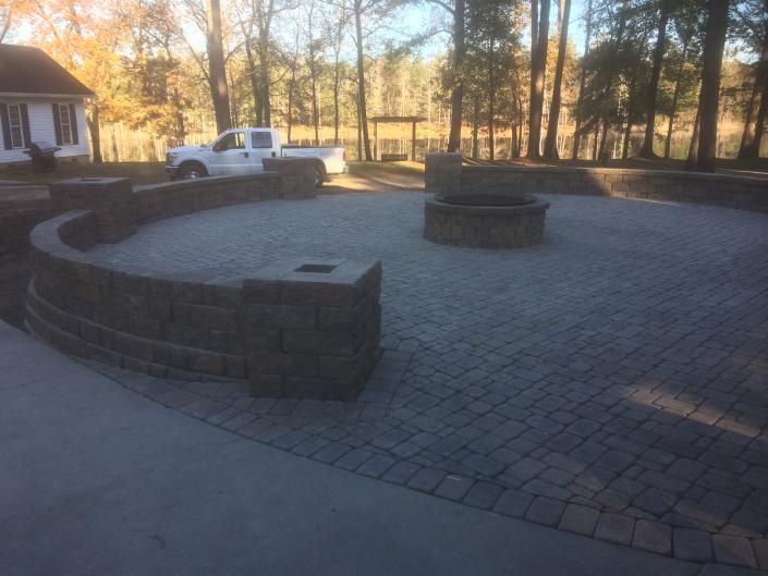 Stone patio with curved wall, fire pit, and a white pickup truck in a wooded area.