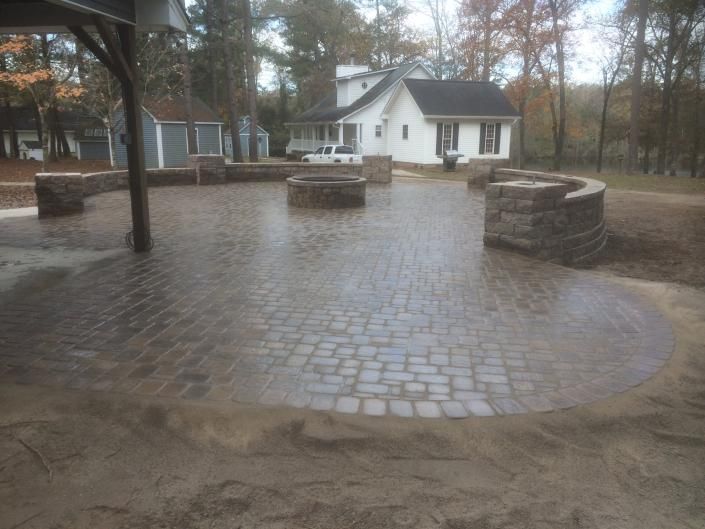 Brick patio with fire pit, seating walls, and a house in the background. Brown, gray, and blue colors.