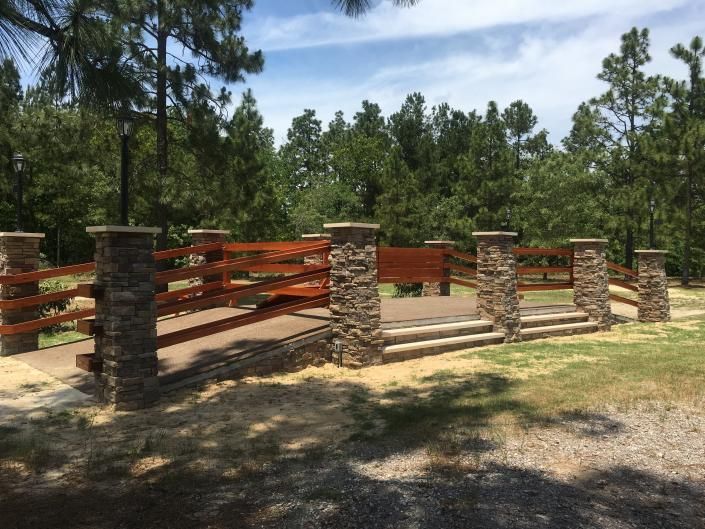 Stone and wood viewing platform in a park. Trees and blue sky in the background.