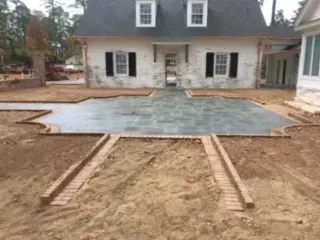 Construction site: a house with brick and concrete patio under construction.  Brown dirt surrounds the unfinished work.