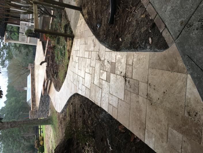Stone pathway curving through a yard, leading toward a building and trees.