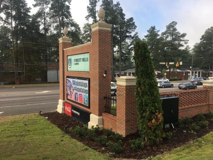 Brick entrance with a digital sign advertising an event, with cars and trees in the background.