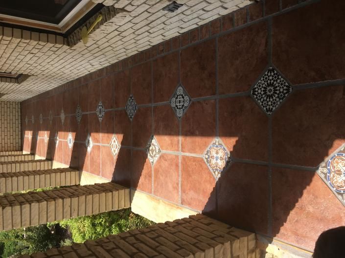 Brown tiled wall with decorative tiles, cast shadows, and brick benches.