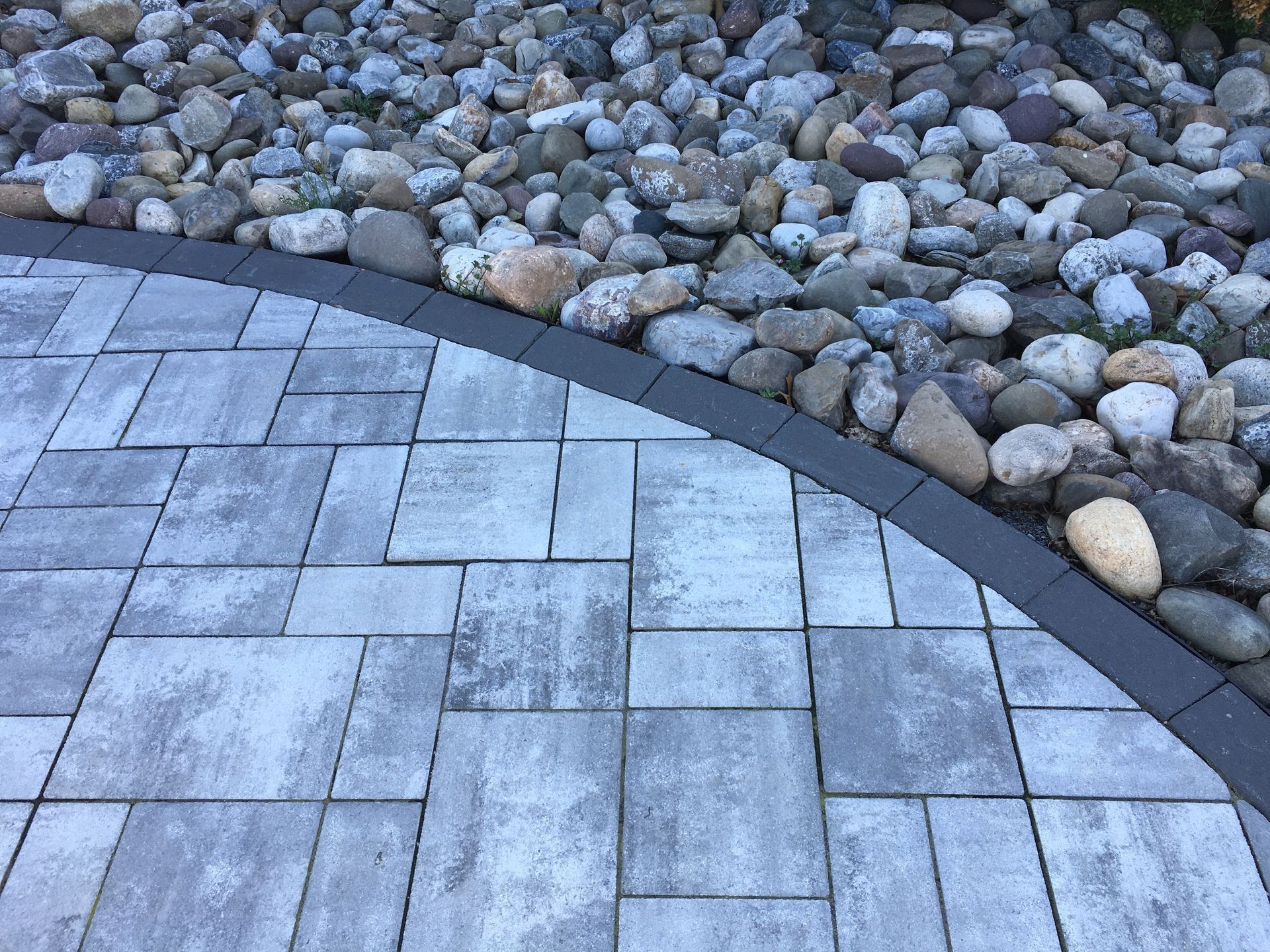 Gray pavers curving to a bed of gray and tan river rocks, separated by a dark border.