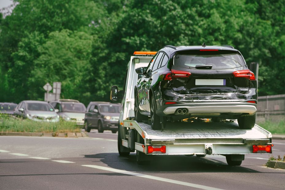 A tow truck is towing a damaged car on a highway.