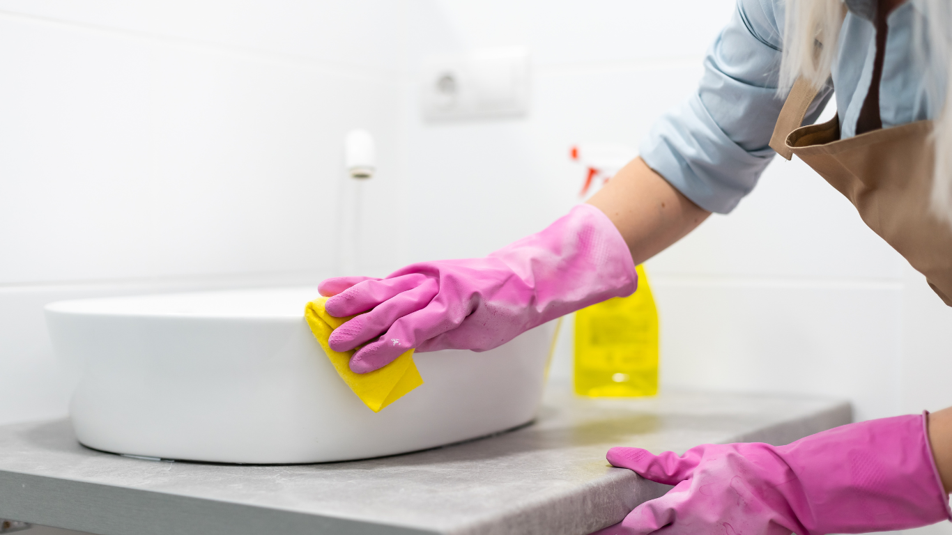 a woman wearing pink gloves is cleaning a bathroom sink .