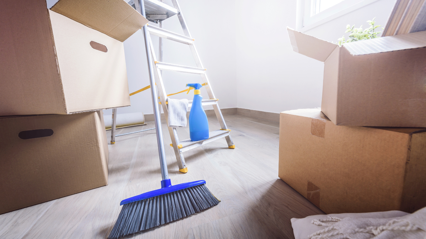 a room filled with boxes , a broom , a spray bottle and a ladder .