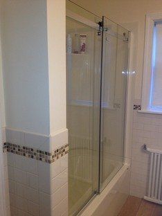 Glass shower door with a metal sliding track installed on a tiled half-wall in a bathroom.