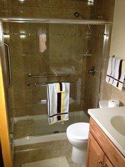 A bathroom with a tiled walk-in shower featuring glass sliding doors, grab bars, a white toilet, and a vanity countertop.