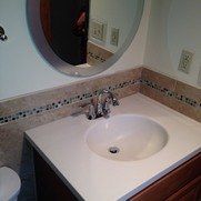 A bathroom vanity with a white countertop, an oval sink, a chrome faucet, and a round mirror with tile backsplashes.