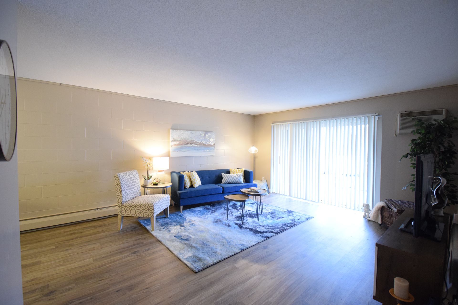 A living room with a blue couch , chairs , coffee table and sliding glass doors.