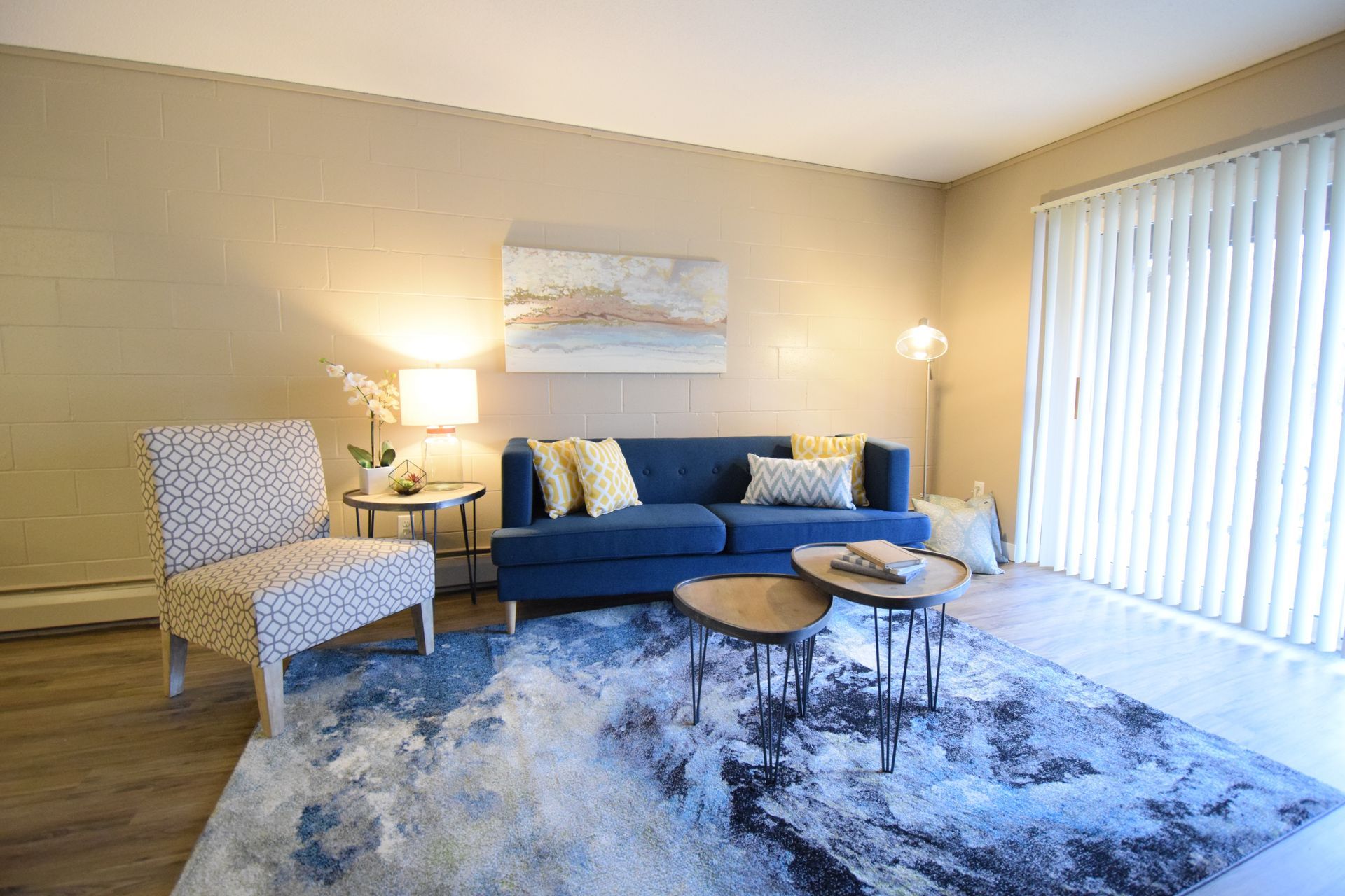 A living room with a blue couch , chairs , tables and a rug.