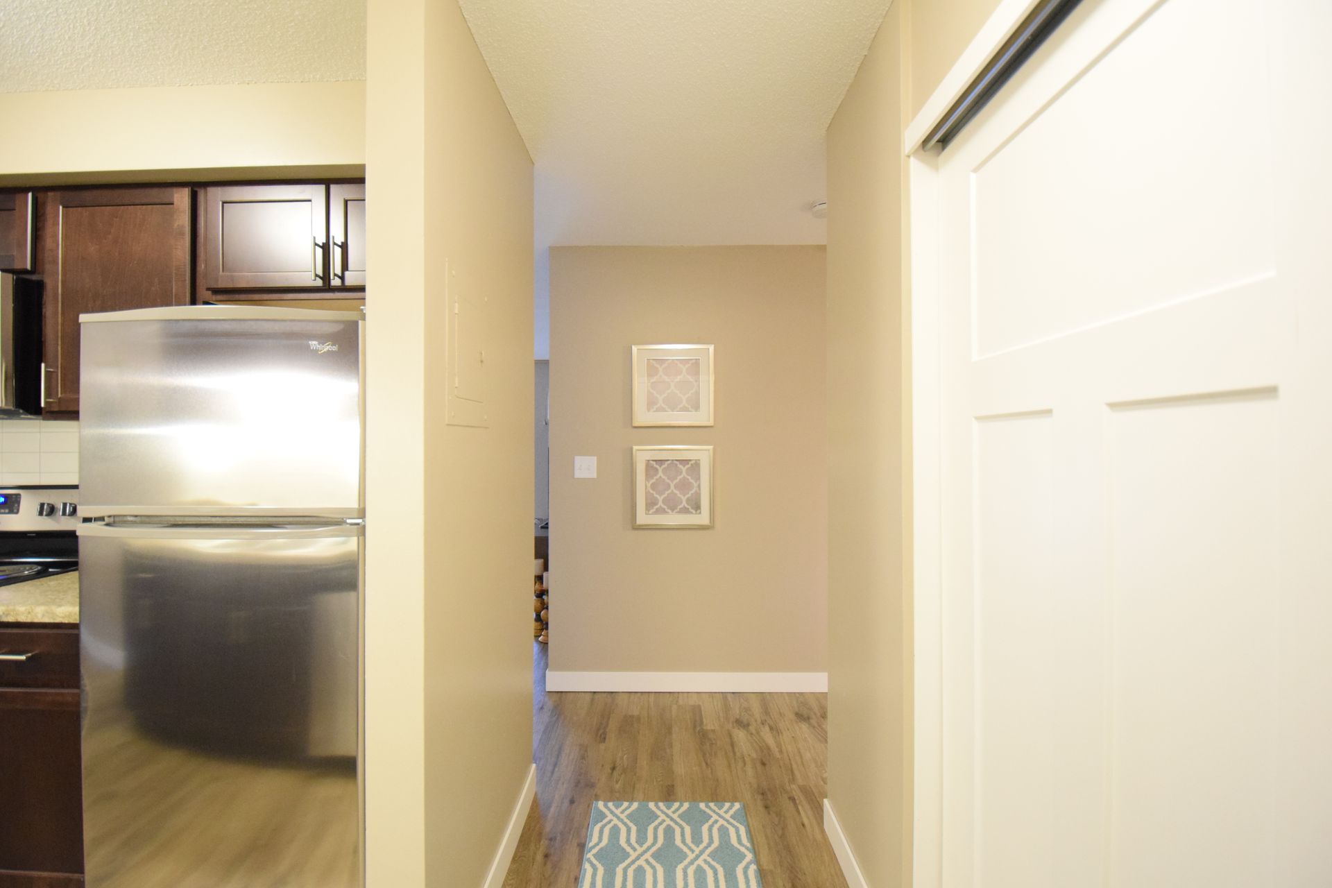 A hallway leading to a kitchen with a stainless steel refrigerator
