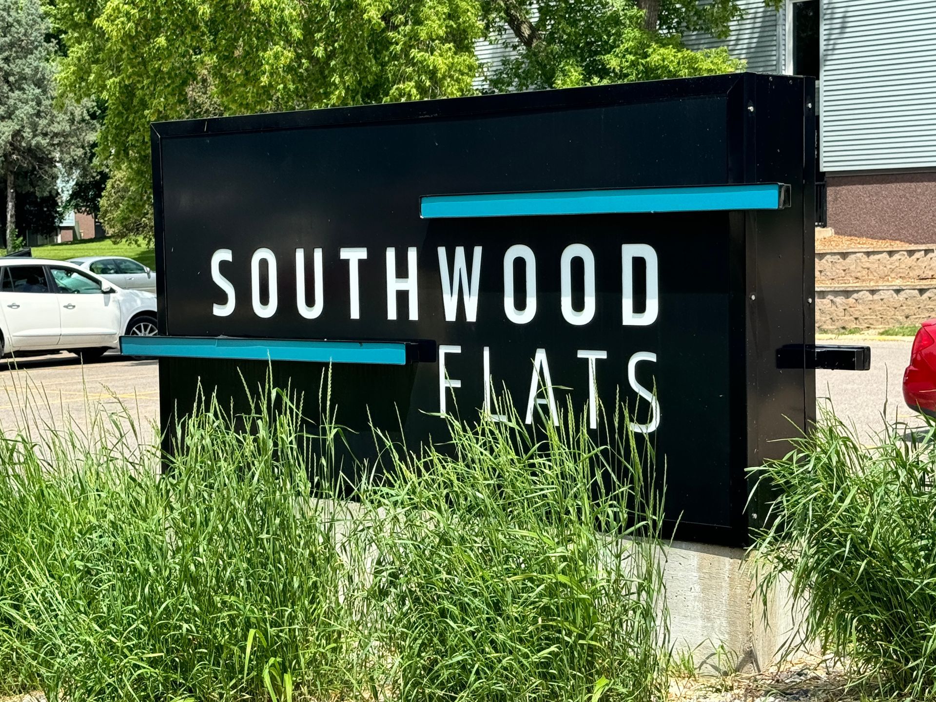 A sign for southwood flats is surrounded by tall grass and trees.