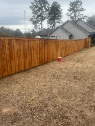 Wooden fence in a yard with a red bucket. Buildings and trees in the background.