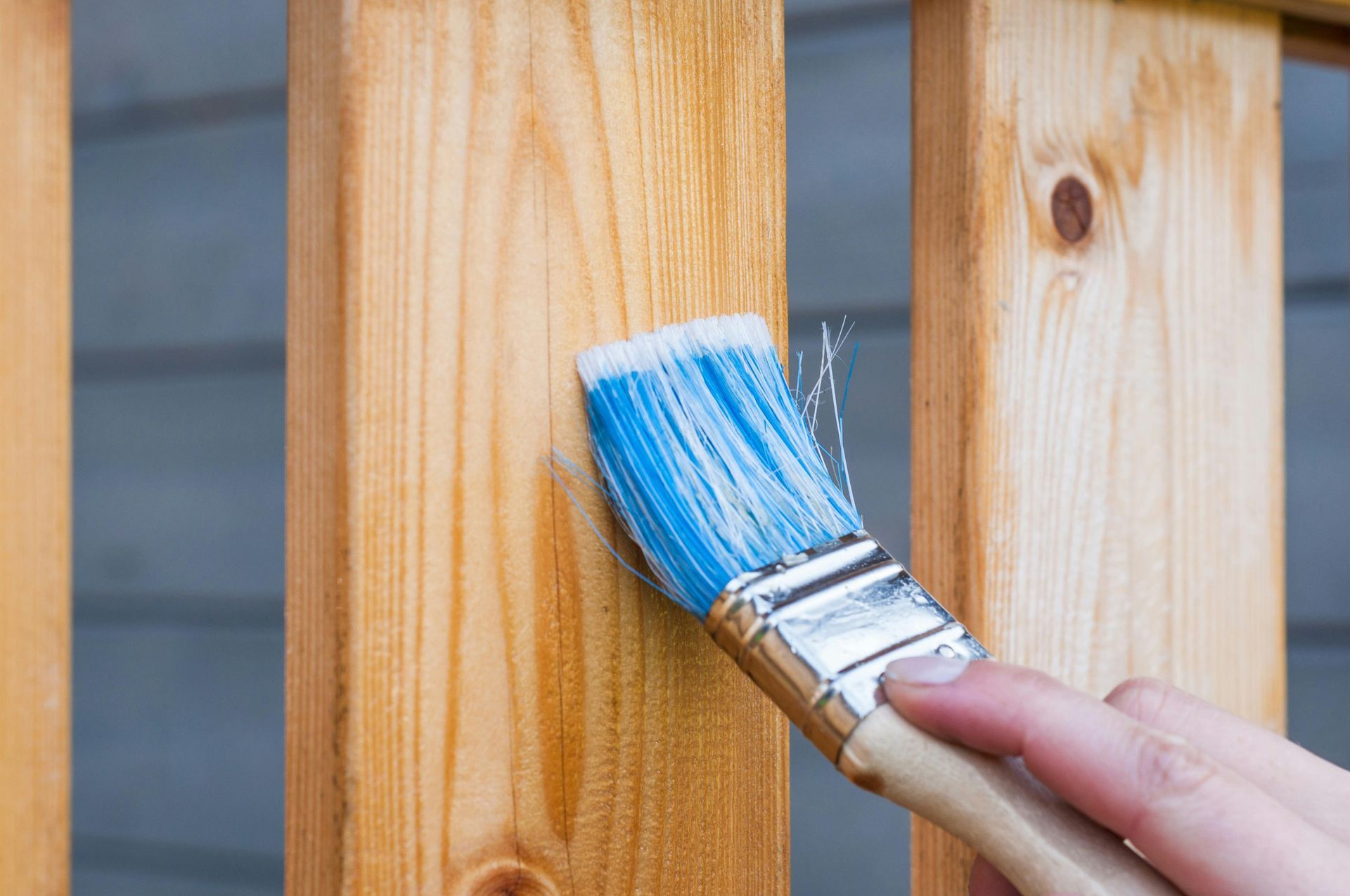 Painting a wooden railing with a blue paintbrush.