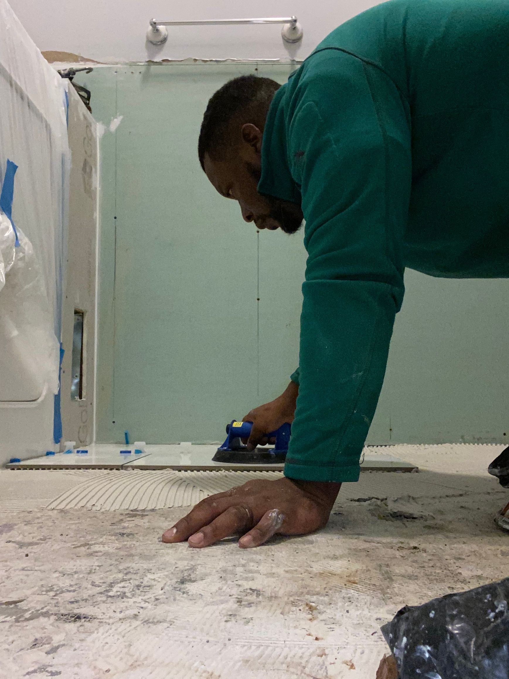 A man in a green shirt is kneeling on the floor using an iron.