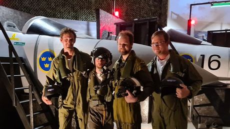 Fyra personer i flygdräkter poserar framför ett svenskt stridsflygplan.