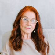 A woman with red hair and glasses is sitting on a couch.