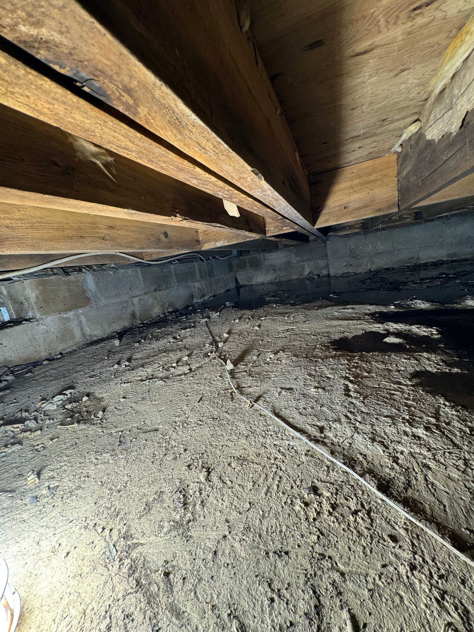 A crawl space with wooden beams and dirt on the floor.