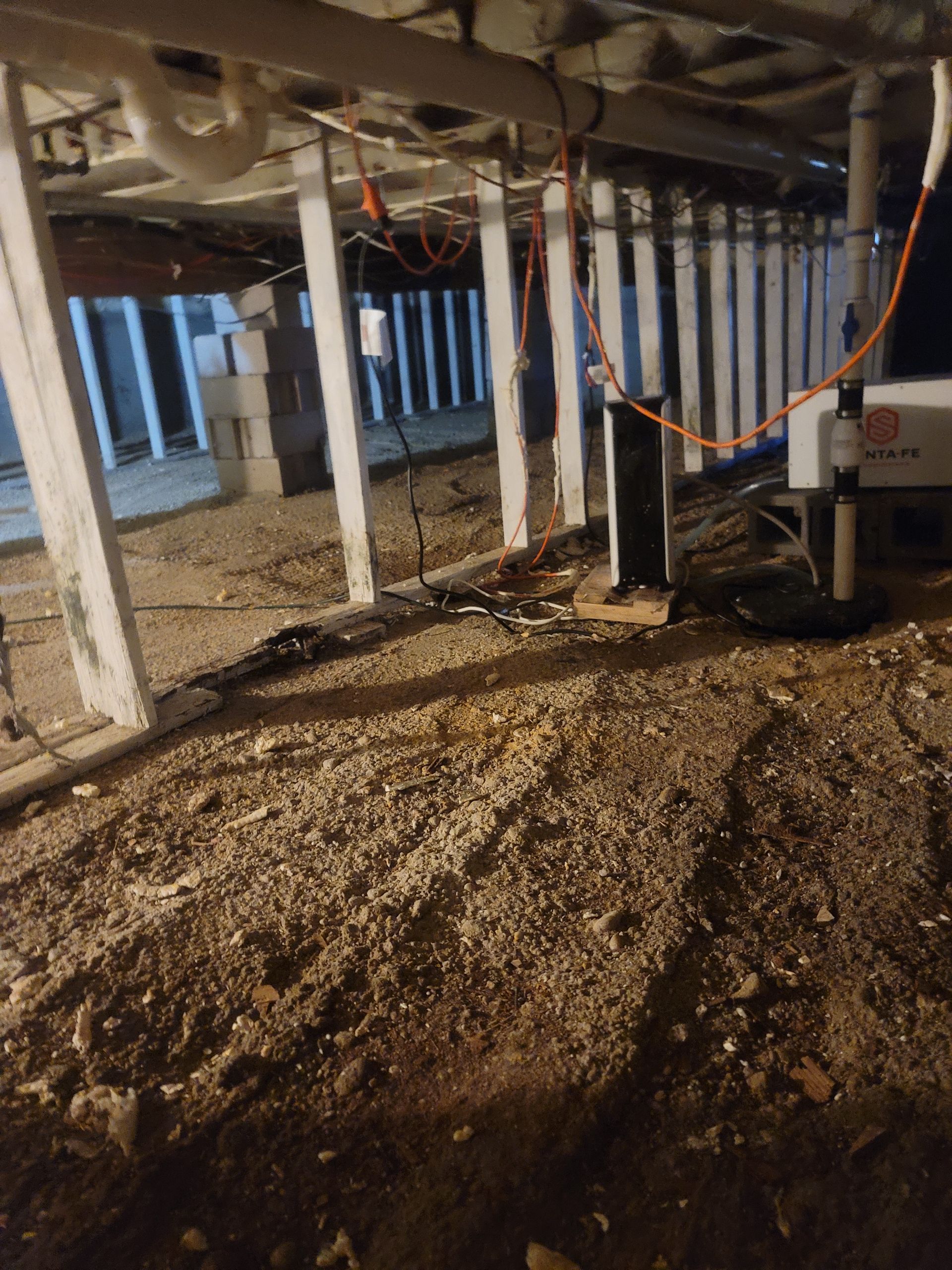 A dirty basement with a lot of dirt and pipes.