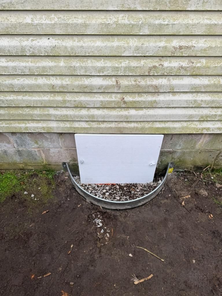 A window well in the ground next to a house.