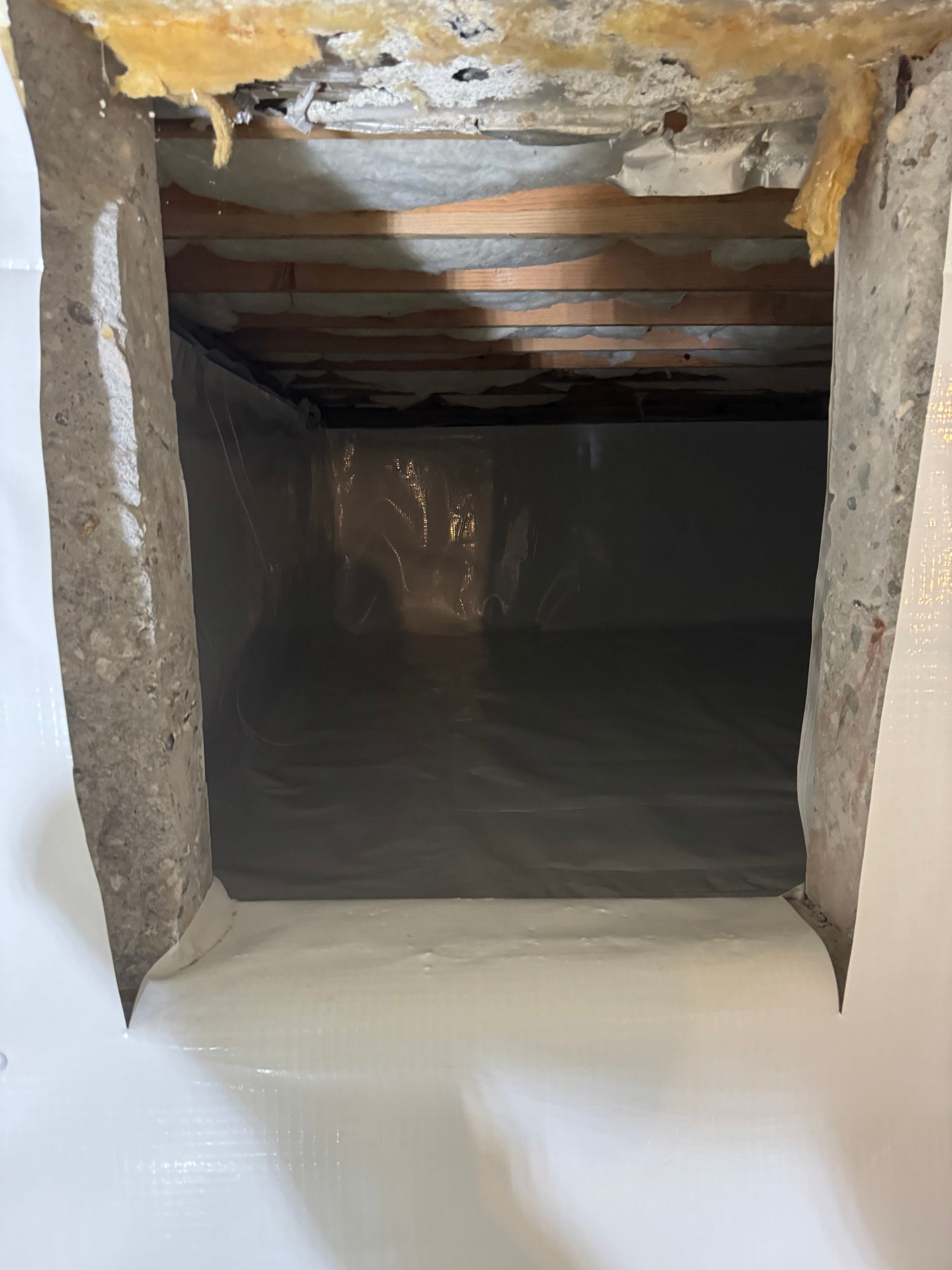 A hole in the ceiling of a basement with plastic covering it.