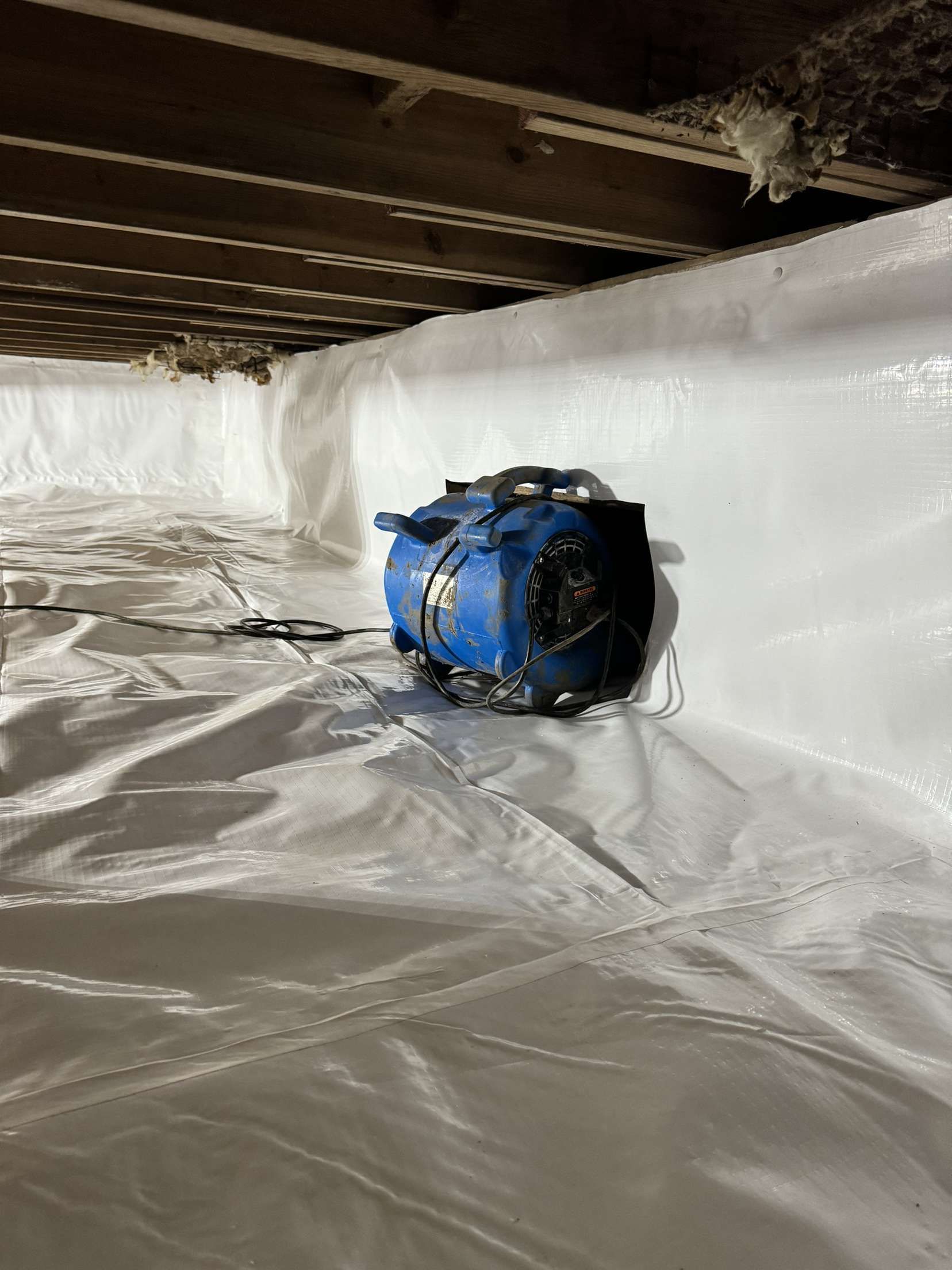 A blue fan is sitting on top of a white tarp in a basement.