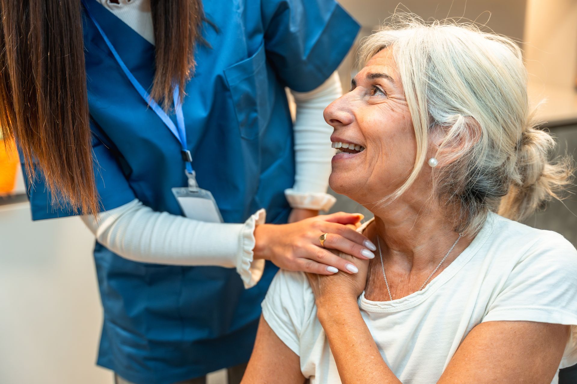 A healthcare worker in a blue uniform gently places a hand on a patient's shoulder, offering a supportive, warm interaction. A healthcare worker in a blue uniform gently places a hand on a patient's shoulder, offering a supportive, warm interaction.