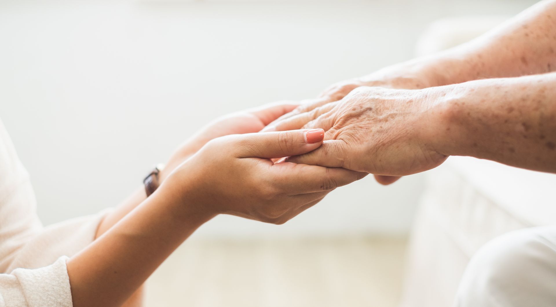 A pair of hands gently holding an older person's hands in a gesture of comfort and support.