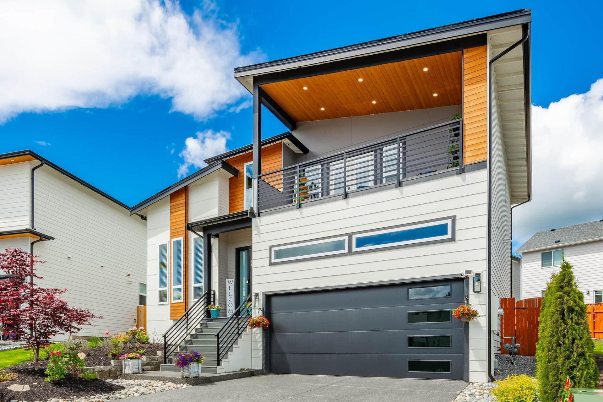 Modern two-story house with a balcony and a gray garage door against a blue sky.