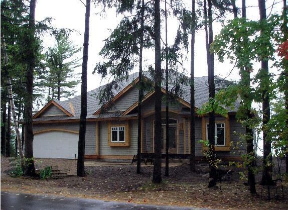 House nestled among trees; exterior view, light gray siding, tan trim, garage door.