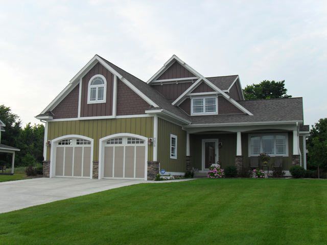 Green house with brown trim and two-car garage, on a green lawn with a driveway.
