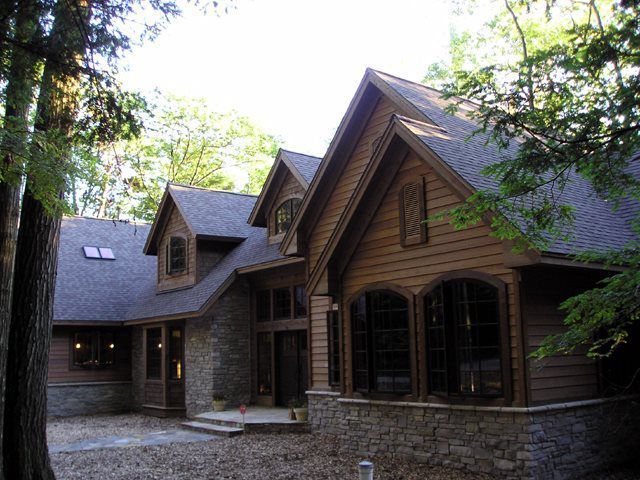 Brown and stone exterior of a large house with multiple gables and large windows surrounded by trees.