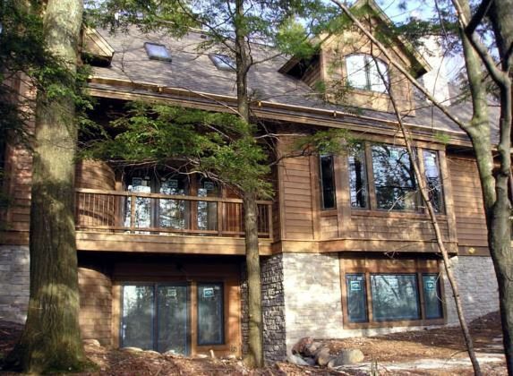 Multi-story wooden cabin with stone foundation, balcony, and large windows set among trees.