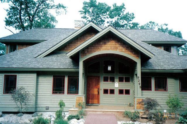 House exterior, Craftsman style, green siding, brown door, arched entry, trees in background.