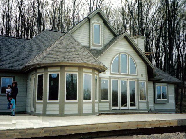 House with round turret and large windows; person holds a child outside.