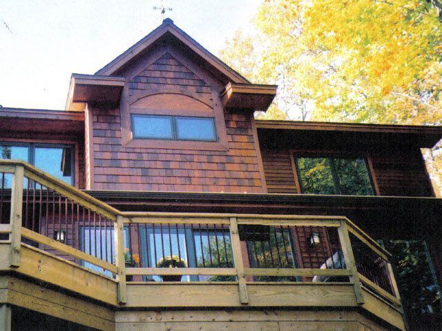 Wood-sided house with a deck, windows, and an arched window on a fall day.